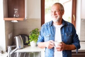 older man holding coffee in kitchen and smiling 