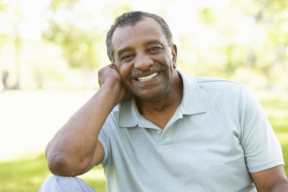 Older man sitting on a park bench smiling while resting his chin on his hand