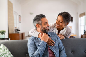 man sitting on couch and his wife is behind him hugging his shoulder